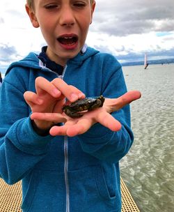 Cute boy holding crab against sea