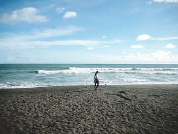 Boy standing on beach against sky