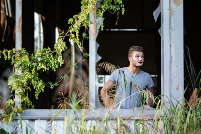 Young man looking away while standing against plants