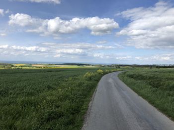 Empty road amidst field against sky