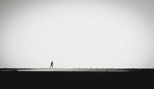 Silhouette man walking on beach against clear sky