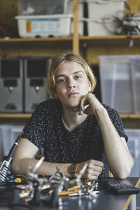 Portrait of confident young male student sitting with science project at desk in classroom at high school