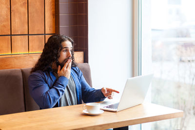 Young woman using mobile phone while sitting on table