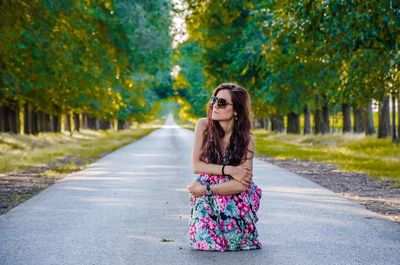 Fashionable woman wearing sunglasses crouching on road