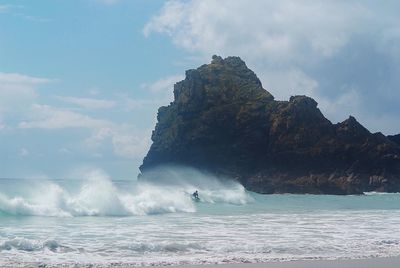 Mid distance view of man surfing on sea against sky during sunny day