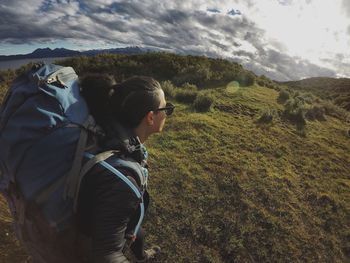 Woman with backpack standing on field against sky