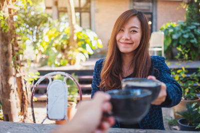 Smiling woman toasting coffee cup with friend at yard