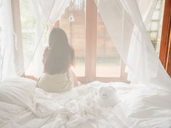 Rear view of woman relaxing on bed at home