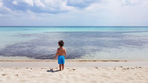 Rear view of boy standing at beach against sky