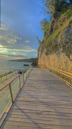 Empty footpath by sea against sky