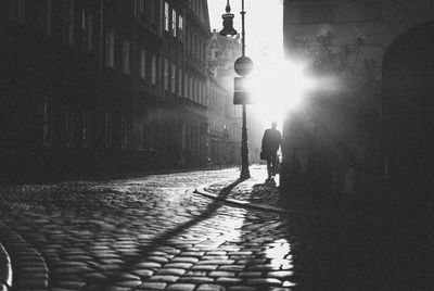 Silhouette person walking on sidewalk by street during sunny day