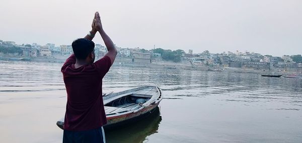 Rear view of man standing on boat in river against sky