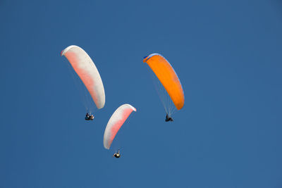 Low angle view of paragliding against clear blue sky