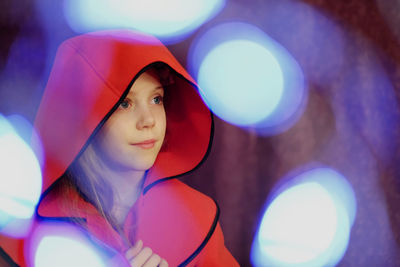 Teenage girl in red hood amidst illuminated lights