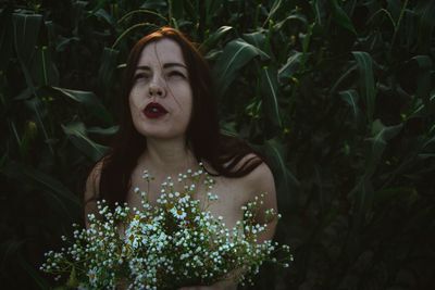 Sensuous woman holding flowers against plants