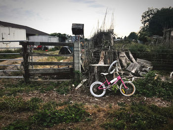 Bicycle parked on field by building against sky