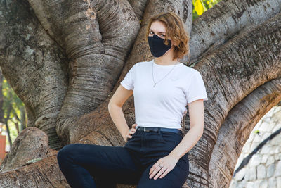 Portrait of young woman while standing against tree