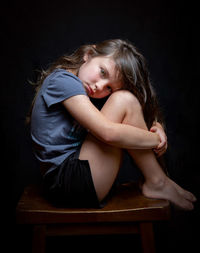 Young woman sitting on chair against black background