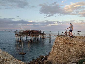 Man riding bicycle on rocks by sea against sky