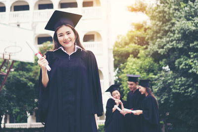Cheerful student in graduation gown standing outdoors