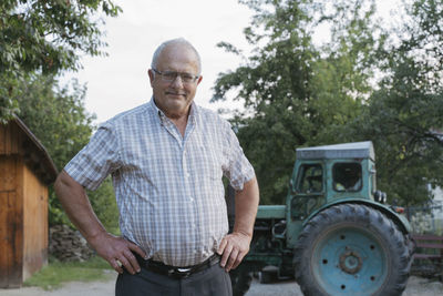 Senior farmer with hands on hips standing in front of tractor