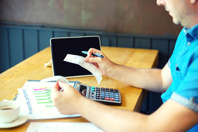 Midsection of man using mobile phone while sitting on table