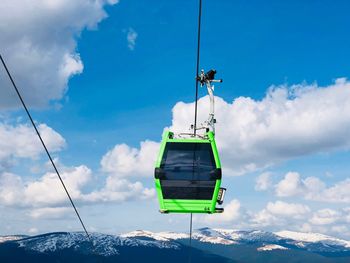 Green gondola lift up in the air over snowcapped mountains on a sunny day with blue sky