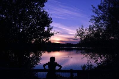 Silhouette man standing in front of lake against sky during sunset