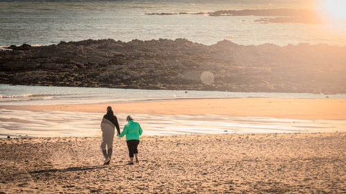 Rear view of men on beach against sky during sunset