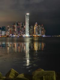 Illuminated buildings by river against sky at night