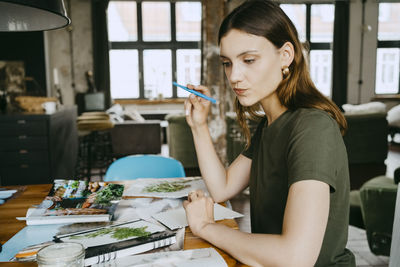 Thoughtful female food stylist puckering lips and holding pen while working in studio