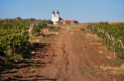 Dirt road by built structure against sky