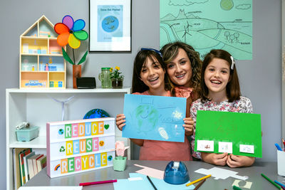 Teacher in classroom looking at camera next to students showing colorful ecological drawings