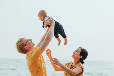 Family enjoying against sea and clear sky