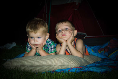 Siblings relaxing by tent on field at night