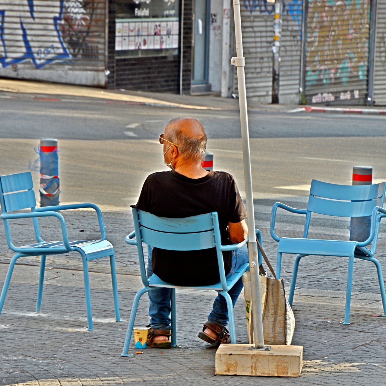 REAR VIEW OF MAN SITTING ON CHAIR AT TABLE IN CITY