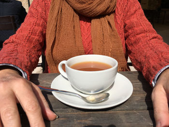 Midsection of woman with coffee sitting on sunny day
