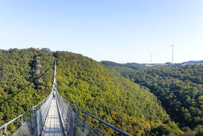 Suspension wooden bridge with steel ropes over a dense forest in west germany, visible tourists. 