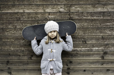 Portrait of girl holding skateboard against wall