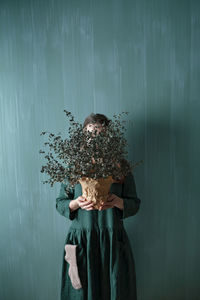 A young woman in a green linen dress making her creative self-portrait against a green wall