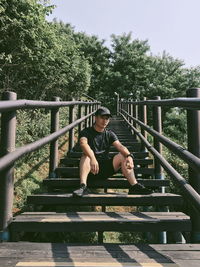 Portrait of young man sitting on railing against trees
