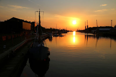 Silhouette boats moored on river against orange sky