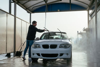 Focused side view of man with hose washing car at washing station