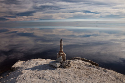 Rocks by lake with clouds reflection against sky