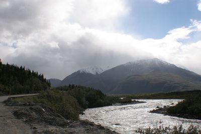 Stream flowing through mountain against cloudy sky