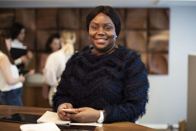 Portrait of smiling female entrepreneur with smart phone at desk