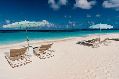 Deck chairs on beach against sky