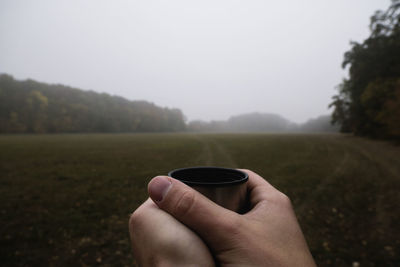 Cropped image of hand holding coffee cup against clear sky