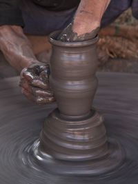 Midsection of man making pottery while sitting outdoors