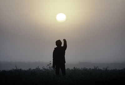 Rear view of silhouette woman standing against sky during sunset